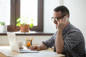 c'est un homme qui téléphone en souriant devant son ordinateur